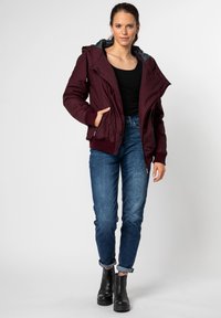 Burgundy zip jacket with a hood, featuring a contrasting gray lining and ribbed cuffs. Worn with blue jeans and black ankle boots.