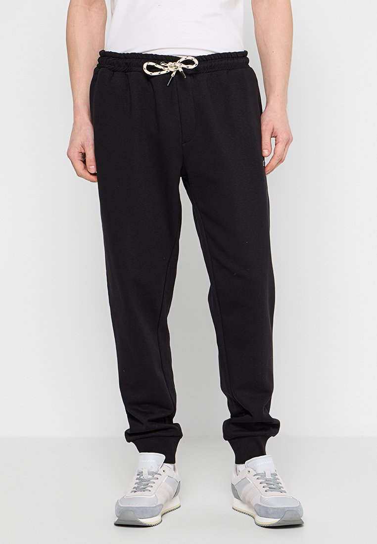 Zwarte sweatpants met een elastische tailleband, trekkoordsluiting en taps toelopende manchetten. Draag ze met grijze en witte sportschoenen.