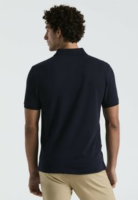 Polo en navy fabriqué à partir d'un tissu texturé, avec un col classique et des manches courtes. Fentes latérales discrètes à l'ourlet.