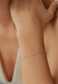 Silver bracelet with a delicate chain design, featuring small accents. Worn on a wrist, highlighting smooth skin texture.