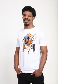 Hvid bomulds t-shirt med et grafisk tryk af en robotfigur med orange og blå accenter, sat mod en ensfarvet baggrund.