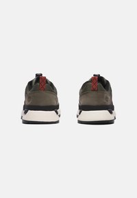 Zapatillas deportivas verdes con detalles negros, materiales de ante y malla, tiradores en el talón y suelas medias blancas. Presentan un detalle en patrón rojo en la parte trasera.