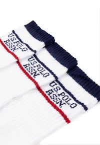 Tre paia di calzini bianchi con bordo blu navy, caratterizzati da strisce rosse e blu navy e con "US POLO ASSN" ricamato in blu navy.