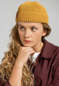 Żółty dzianinowy beret z prążkowanym wzorem i brązową skórzaną metką. Kształt jest dopasowany i ma zaokrąglony wierzch.