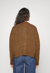 Brun stickad tröja med avslappnad passform, rund hals och ribbad textur. Bakpartiet har en något croppad fåll och sänkta axlar.