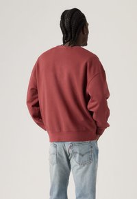 Κόκκινο φούτερ με στρογγυλή λαιμόκοψη και αυτοτραβηγμένους ώμους, με ριμπ μανσέτες και τελείωμα. Συνδυασμένο με ανοιχτόχρωμο τζιν.