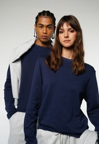 Navy long-sleeve shirts, one paired with a gray hoodie, feature crew necklines and a relaxed fit, with soft fabric and minimal details.