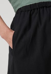 Svarta byxor med elastisk midja och sidficka, tillverkade av ett mjukt, texturerat tyg med en avslappnad passform.