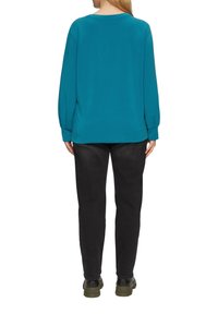 Türkiser, oversized Sweatshirt mit langen Ärmeln, rundem Halsausschnitt und gerippten Bündchen, kombiniert mit dunklen, slim-fit Hosen und schwarzem Schuhwerk.