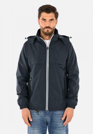 Giacca impermeabile blu navy con zip e dettagli bianchi, tasche con zip, polsini elasticizzati e cappuccio pieghevole. Texture liscia.