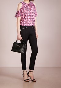 Blusa floreale a spalle scoperte in rosa, pantaloni neri con dettagli zip, borsa nera trapuntata e tacchi neri con cinturini. Texture del tessuto liscia.