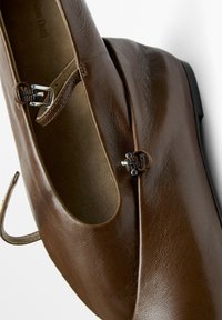 Brown leather Mary Jane shoe with silver buckle straps on a white background, showing the side and top view.