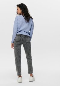Pull en tricot bleu clair associé à un jean noir délavé taille haute. Des baskets blanches complètent la tenue, avec des détails visibles sur les poches arrière.