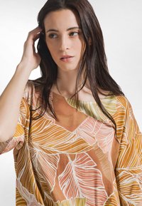 Løs bluse i brun med store bladmotiver i nuancer af orange og hvid. Glat tekstur med en bred halsudskæring.