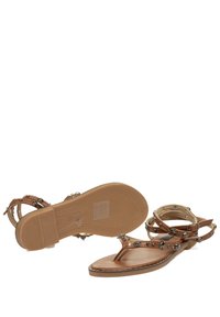 Sandalias planas marrones con diseño de tira entre los dedos, con correas entrelazadas adornadas con acentos metálicos circulares y una suela texturizada.
