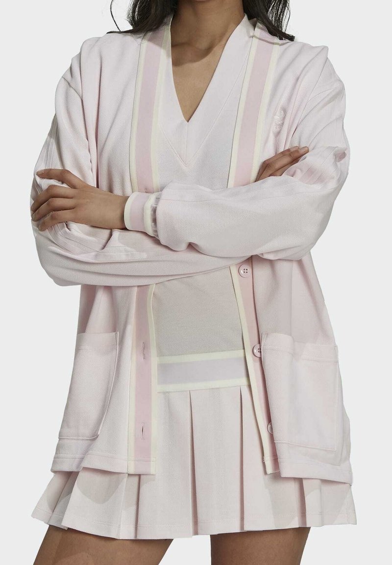 Ljusrosa kofta med V-ringning, med vita och blekrosa ränder. Den har en avslappnad passform, knappstängning framtill och sidofickor.