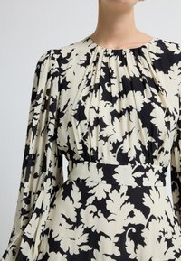 Vestido floral con patrones de hojas en blanco y negro, cuello plisado y mangas largas y fluidas; hecho de tejido ligero.