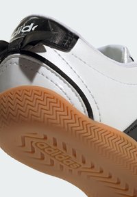 Gros plan sur le talon et la semelle d'une basket blanche Adidas avec des accents noirs et une semelle extérieure en caoutchouc marron texturée.