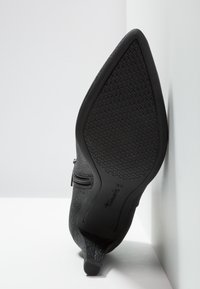 Stivale alla caviglia nero con suola in gomma testurizzata, dettaglio con zip e parte superiore simile alla camoscio, dotato di un tacco basso e leggere rifiniture luminose.