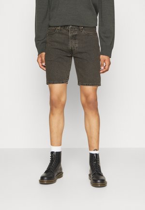 Shorts en denim noir à coupe droite, texture délavée et coutures contrastantes. Associés à des bottes noires à lacets et des chaussettes blanches.
