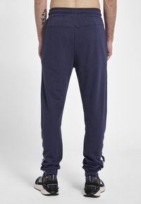 Marineblaue Freizeit-Hosen mit einer entspannten Silhouette, elastischem Taillenbund und gerafften Knöcheln. Kombiniert mit schwarzen Freizeitschuhen mit blauen Akzenten.