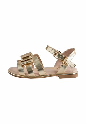 Goldene flache Sandale mit mehreren Riemen, einer metallischen Schnalle und einer dekorativen Schleife am vorderen Riemen, entworfen für Frauen.