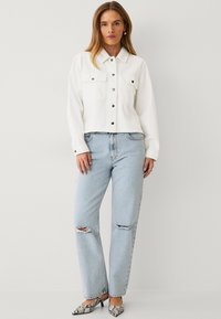 Hvid cropped denimjakke med to brystlommer og trykknapper, parret med lyseblå ripped jeans og mønstrede højhælede sko.