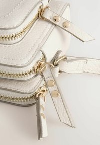 Bolso de cuero texturizado blanco con detalles de cremallera dorada, múltiples compartimentos con cremallera y correas ajustables. Incluye detalles de hardware notables.