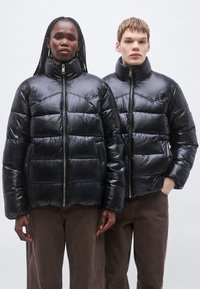 Čierne prešívané bundy s lesklým povrchom, s horizontálnymi prešívanými panelmi a vysokými goliermi. Zips na zapínanie a viditeľné bočné vrecká.