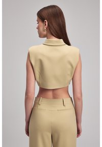 Beige cropped top met een gestructureerde kraag, voorzien van hoekige armsgaten en een gladde textuur. Gecombineerd met een hoge taille bijpassende broek.