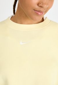 Felpa giallo chiaro realizzata in morbido tessuto, con scollo rotondo a costine e un piccolo logo Nike bianco ricamato sul petto.