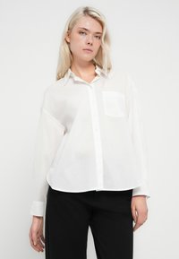 Camisa blanca abotonada hecha de tela ligera. Cuenta con un cuello clásico, un bolsillo único en el pecho y un ajuste relajado con mangas largas.