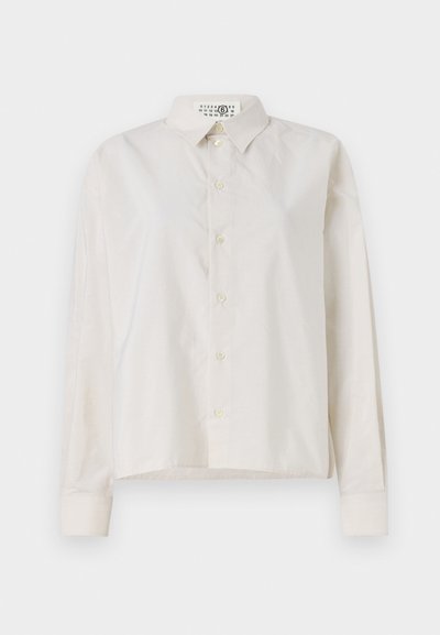 Light beige button-up shirt with a collar, long sleeves, and a slightly textured fabric. Features a row of buttons and a straight hem.