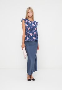 Blå blus med blommönster och volangdetaljer på ärmarna, tillsammans med en lång blå kjol och en rosa clutch, kompletterad med svarta ballerinas.
