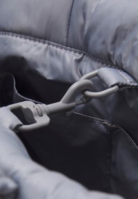 Tissu isolant gris avec une texture lisse, comportant un clip en crochet gris et des coutures visibles le long des bords, à l'intérieur d'une pochette.