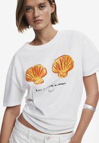 Hvid bomulds t-shirt med orange muslingeillustrationer og teksten "LIVET ER BEDRE OM SOMMEREN," med en afslappet og løs pasform.