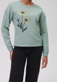 Mátově zelená mikina s kulatým výstřihem, ozdobená černým květinovým vzorem s zlatými prvky. Měkká textura, žebrované manžety a lem.