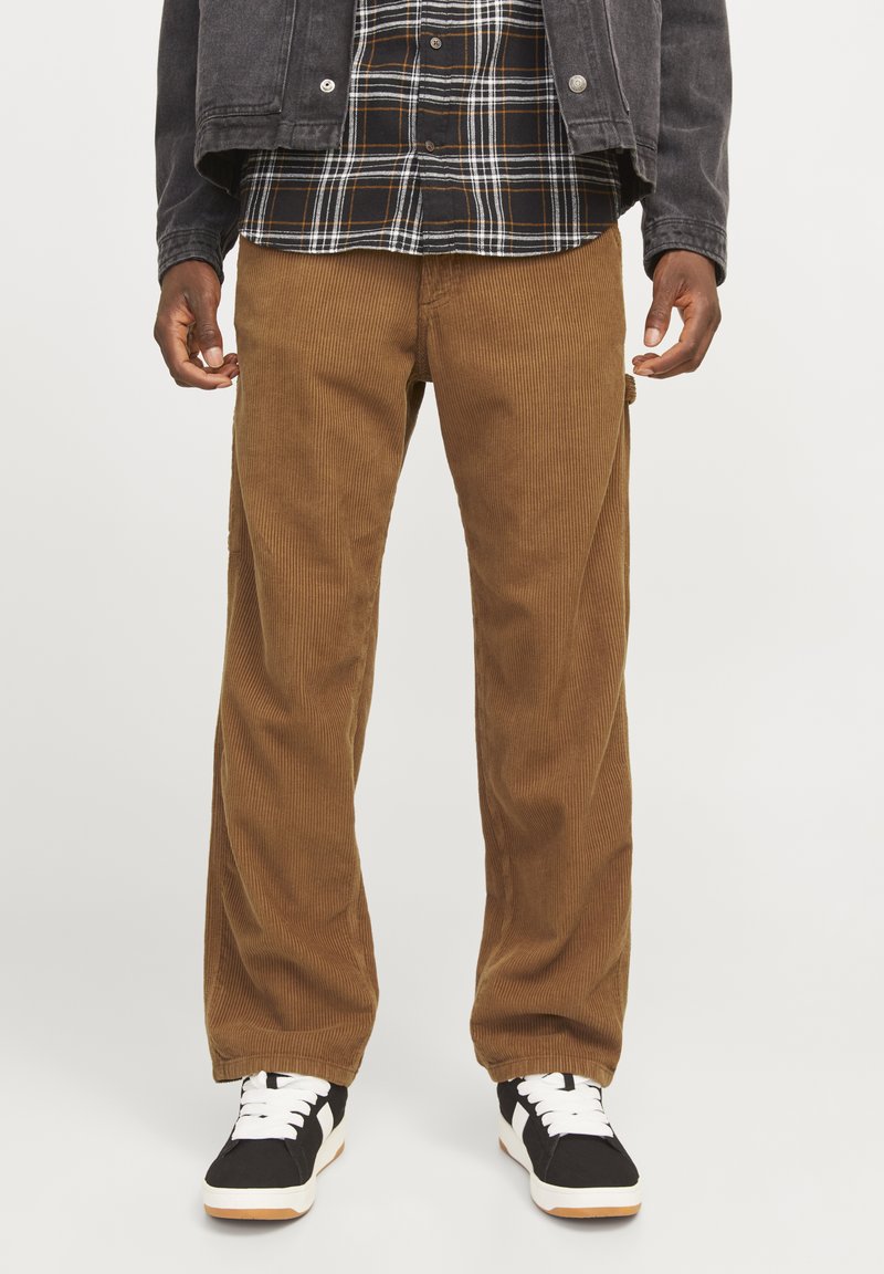 Brown corduroy pants with a straight cut, featuring vertical ribbing and front pockets. Paired with a black and white plaid shirt and black sneakers.