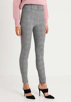 Pantalon slim gris à carreaux avec taille haute et ceinture assortie, associé à des mules noires à talons hauts et un pull en maille rose.
