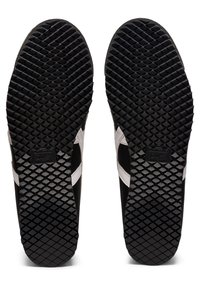 Mustat kuminmukaiset pohjat, joissa on teksturoitu timanttikuvio, valkoiset sivuviivat ja musta logo. Liukas pinta yhdessä kestävän muotoilun kanssa.