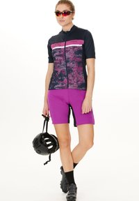 Cykelsæt med en kortærmet navy top, der har et pink mønstret panel, og matchende lilla shorts, suppleret med en sort hjelm.