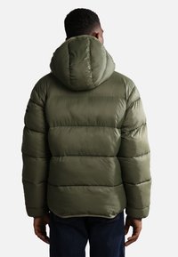 Giacca a vento in verde oliva, con cappuccio, design trapuntato e orlo leggermente curvo; il materiale appare morbido e imbottito.