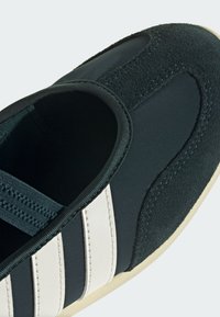 Chaussure de sport noire avec des rayures blanches, une bande élastique et une semelle beige, vue de dessus en se concentrant sur le dessus et la zone des orteils.
