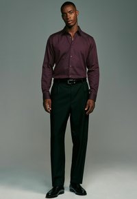 Bordeaux farbenes, gemustertes Hemd mit Kragen, kombiniert mit schwarzen Hosen. Slim-Fit-Design, lange Ärmel mit Knopfmanschetten, getragen mit schwarzen Schuhen.