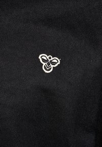 Białe, haftowane logo pszczoły na teksturowanym czarnym tle z tkaniny, wyśrodkowane i wyraźnie widoczne.