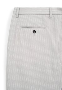 Un pantalon rayé gris clair en tissu doux présente une poche arrière avec un bouton noir et des passants de ceinture supplémentaires à l'avant.