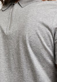 Polo grigio con chiusura a zip e colletto a coste. Il tessuto ha una texture liscia e una silhouette aderente.