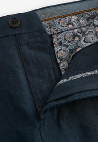 Pantaloni bleumarin dintr-un material texturat, cu fermoar și închidere cu nasture. Talie cu căptușeală interioară cu model floral.