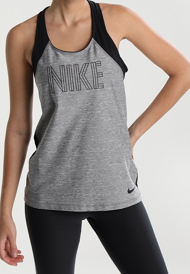 Canotta atletica grigia con spalline nere e logo "NIKE" in lettere nere in grassetto. Il tessuto ha una texture liscia. Abbinata a leggings neri.