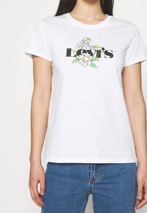 White t-shirt with "Levi's" text and daisy flowers printed on front, worn with blue jeans, torso and arms visible.